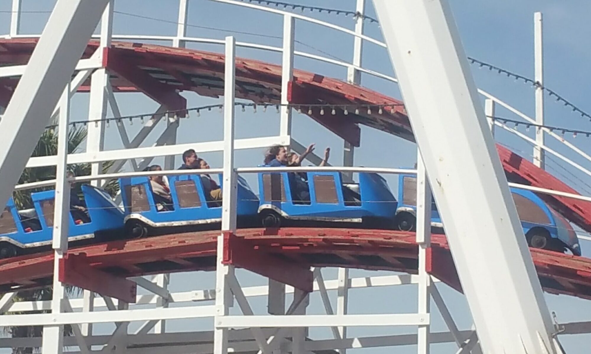 Photo showing people on a roller coaster; one person has hands raised.